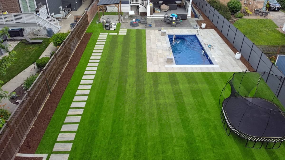 Turf installation in a large backyard with a pool and paver patio installation